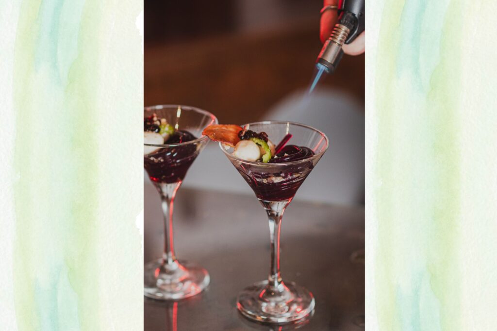 Dois coquetéis de A Alquimista com guarnições e o uso de maçarico, ilustrando a apresentação moderna do Jantar de Drinks e a fusão de mixologia e gastronomia molecular.
