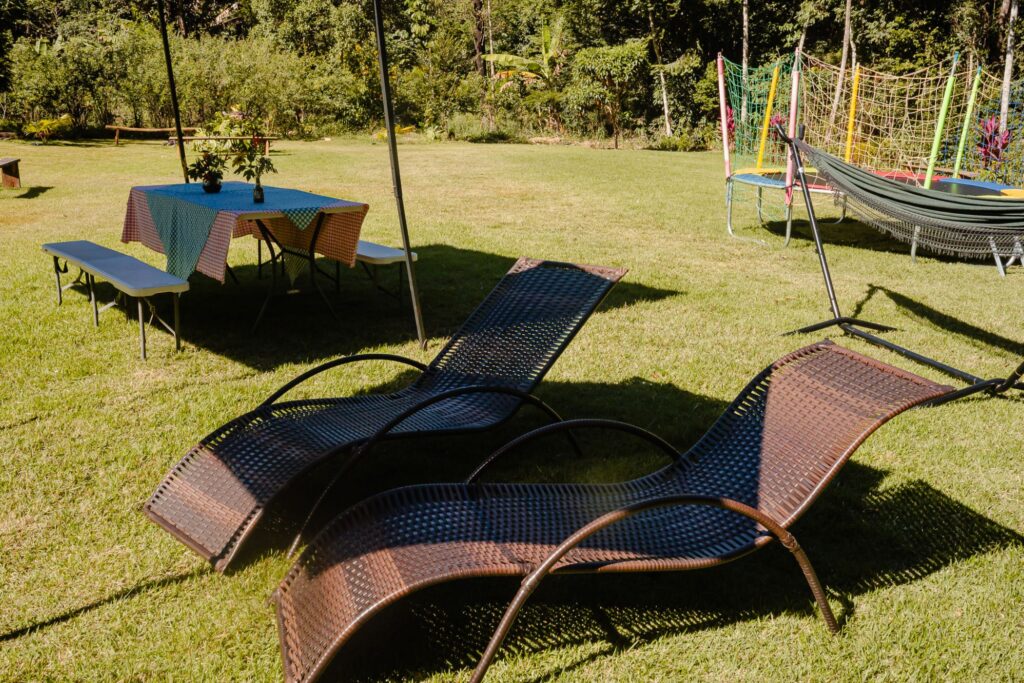 Duas espreguiçadeiras confortáveis em um gramado verde da Ecovila Coração da Mata, com área de convivência ao fundo, ideal para relaxamento.