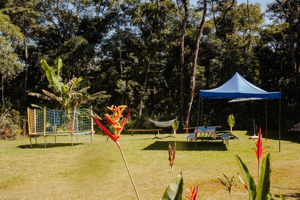 Ampla área verde da Ecovila Coração da Mata com gramado, árvores tropicais, flores coloridas.