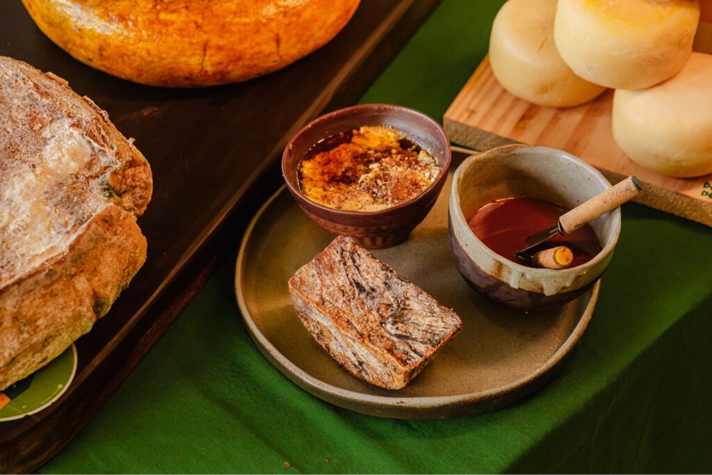 Mesa farta exibindo a variedade de produtos oferecidos na degustação do Aprisco Chèvrèmon, incluindo queijos, pães e doces de leite de cabra.