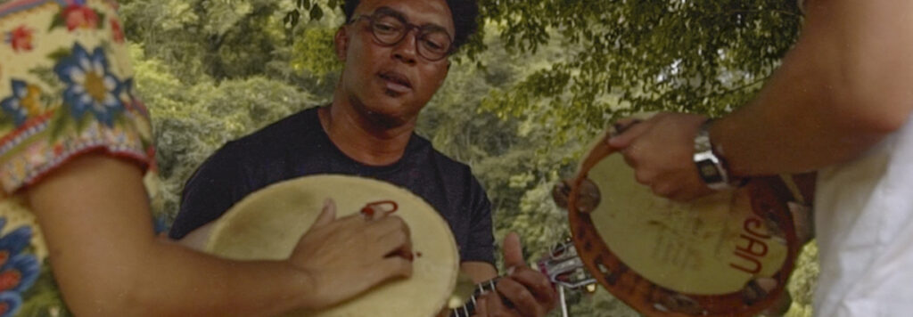 Márcio Nagô tocando violão acompanhado por percussionistas em Brumadinho. 